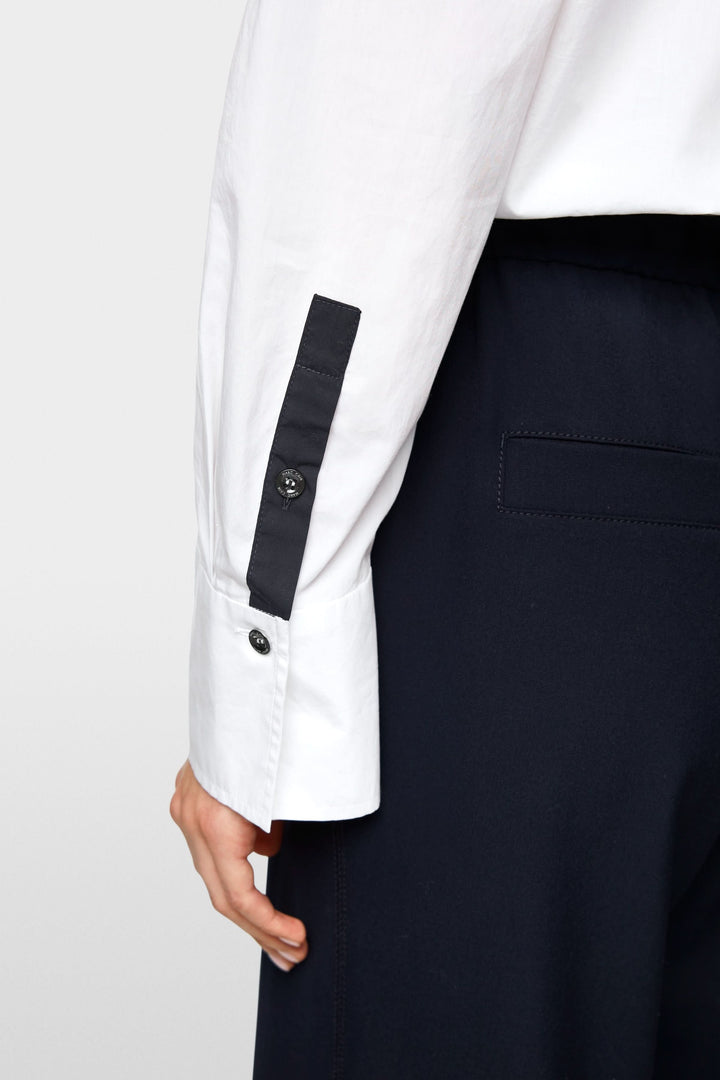 Détail de la manche d'une chemise blanche avec boutons contrastants sur un pantalon noir.