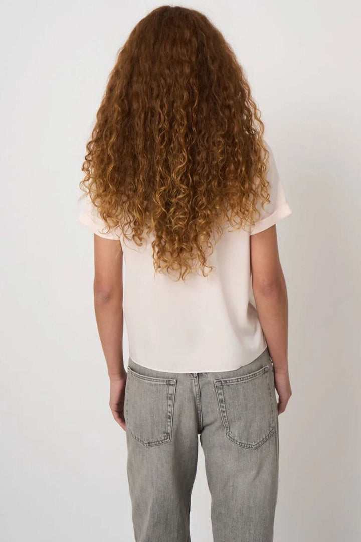 Personne portant une blouse en soie extensible de dos, avec manches courtes à revers et jeans, montrant le style chic et décontracté.