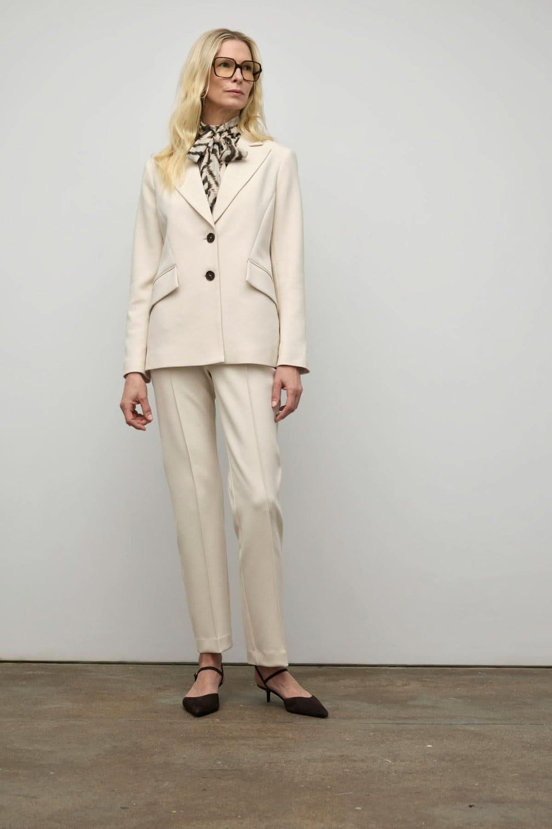 Femme portant un veston semi-ajusté beige avec pantalon assorti et foulard noir, style élégant et professionnel.
