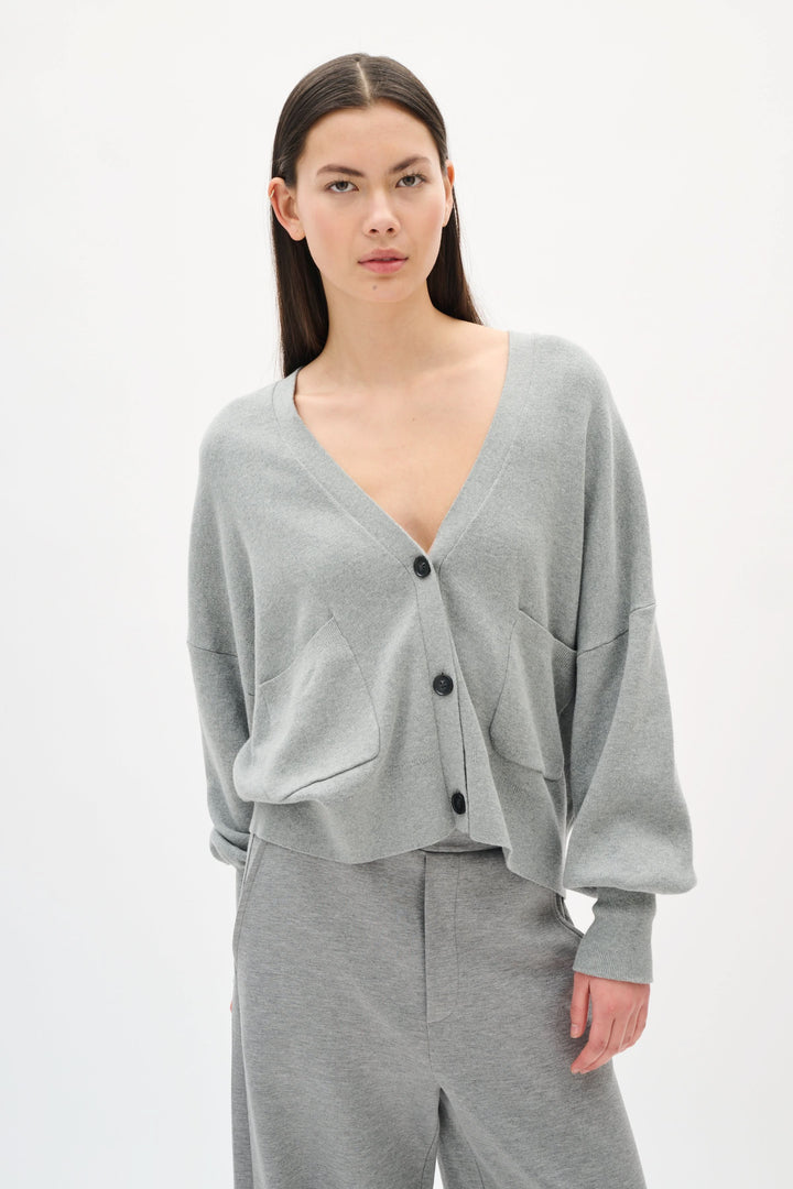 Cardigan Tenley ample en gris avec encolure en V, poche avant et boutons contrastants, porté avec pantalon gris.