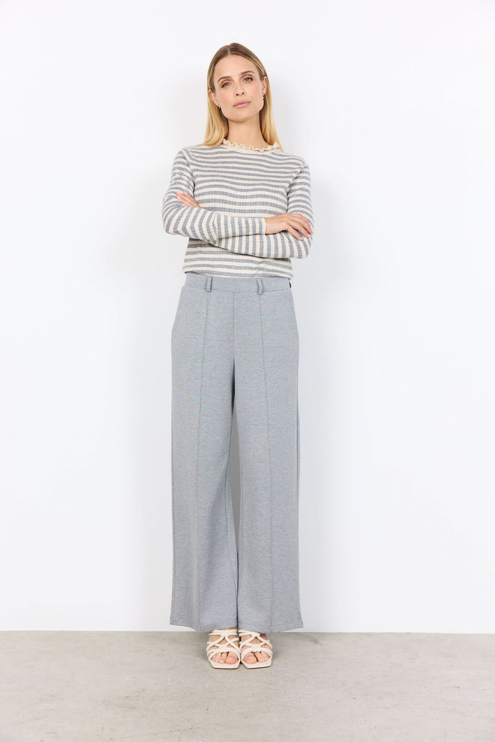 Femme portant un chandail à rayures fines et un pantalon gris, stylé et élégant pour un look sophistiqué.