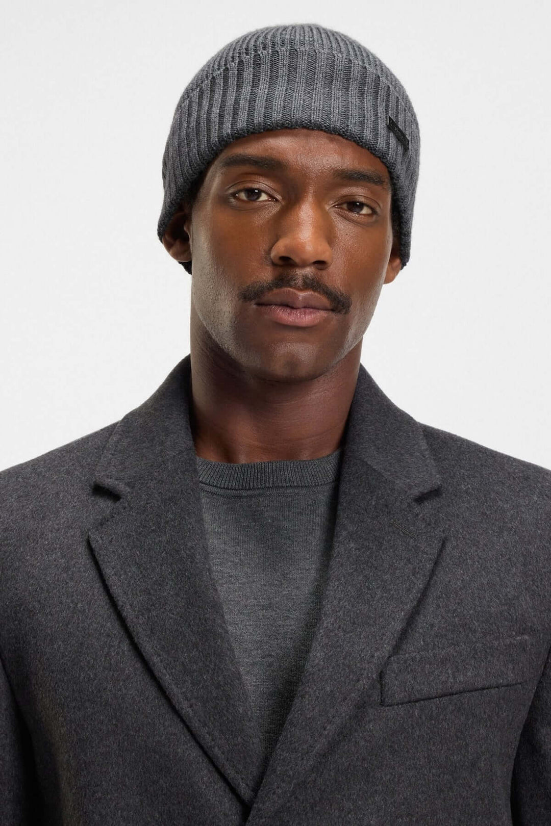 Homme portant une tuque en laine vierge à maille épaisse BOSS, grise, avec un logo en tissu, style élégant pour l'hiver.