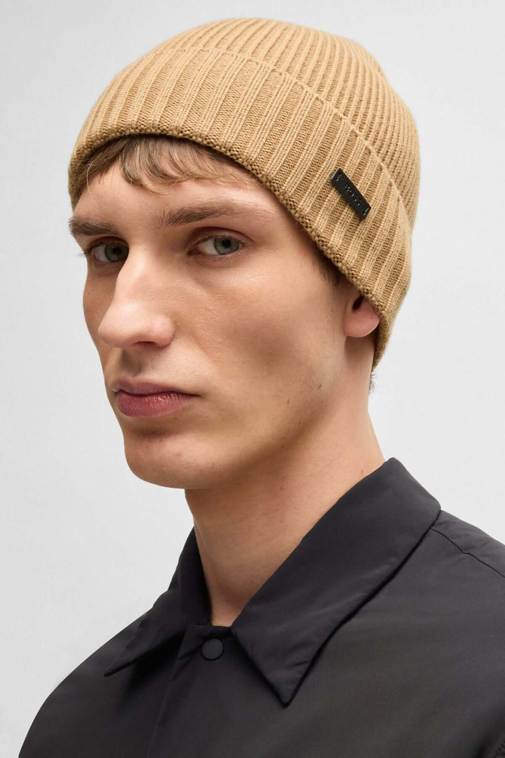 Homme portant une Tuque en laine vierge à maille épaisse BOSS beige avec logo en tissu enduit.