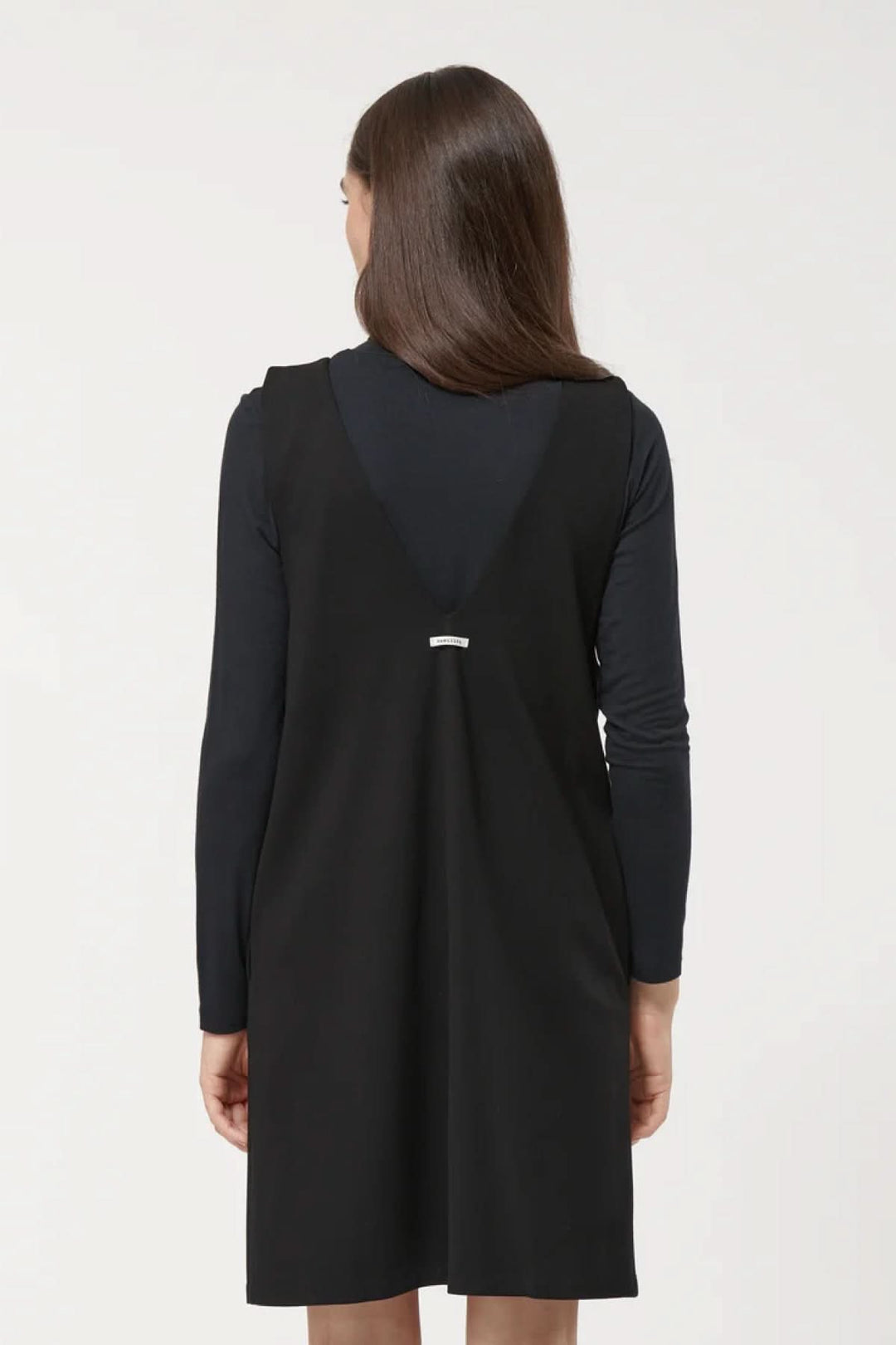 Femme portant une robe sans manches noire à encolure en V, coupe trapèze, sur un sous-pull noir.