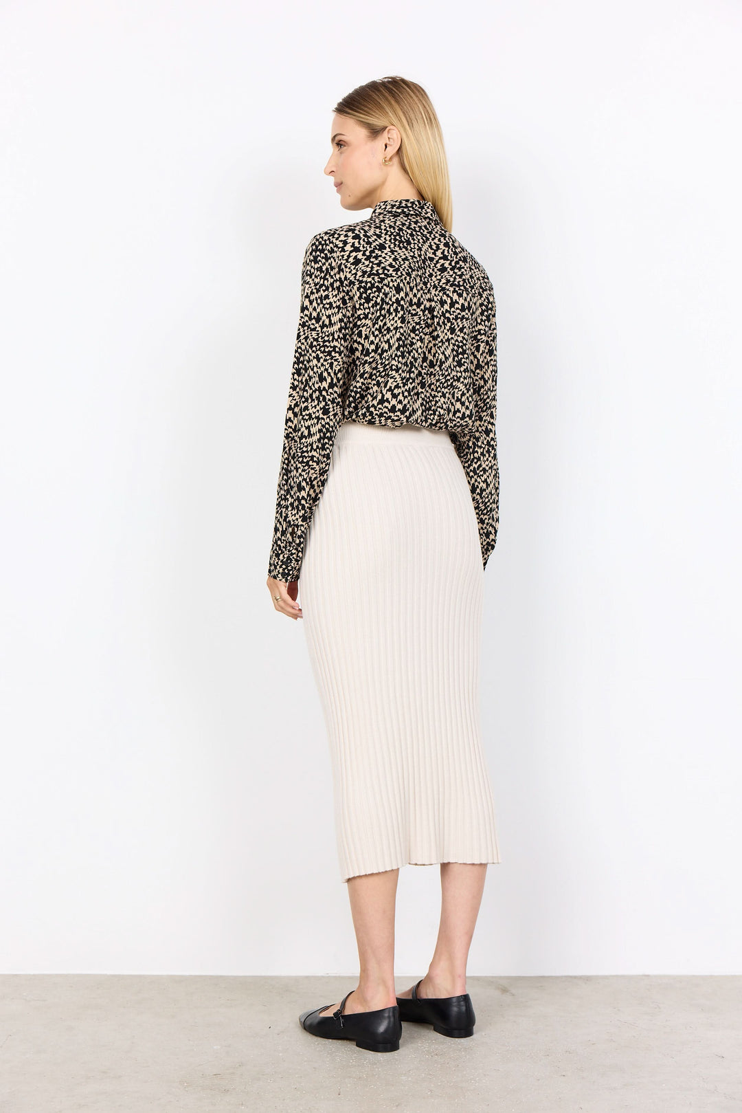 Femme de dos portant une jupe midi en maille côtelée beige et un haut à motif animalier, style moderne.