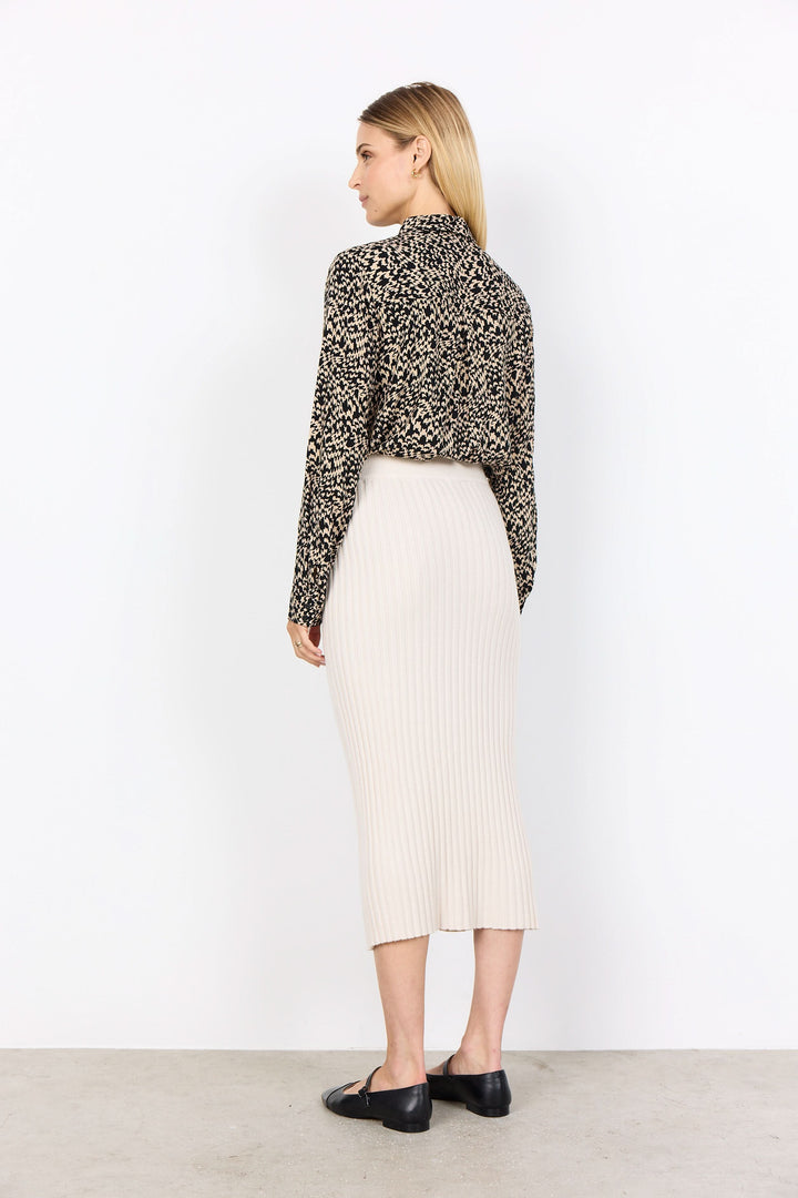 Femme de dos portant une jupe midi en maille côtelée beige et un haut à motif animalier, style moderne.