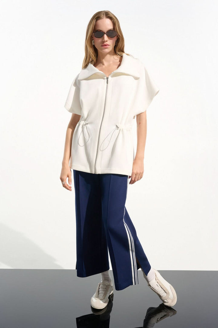 Veste zippée à col large moderne avec col structuré, portée par un modèle en pantalon bleu ample.