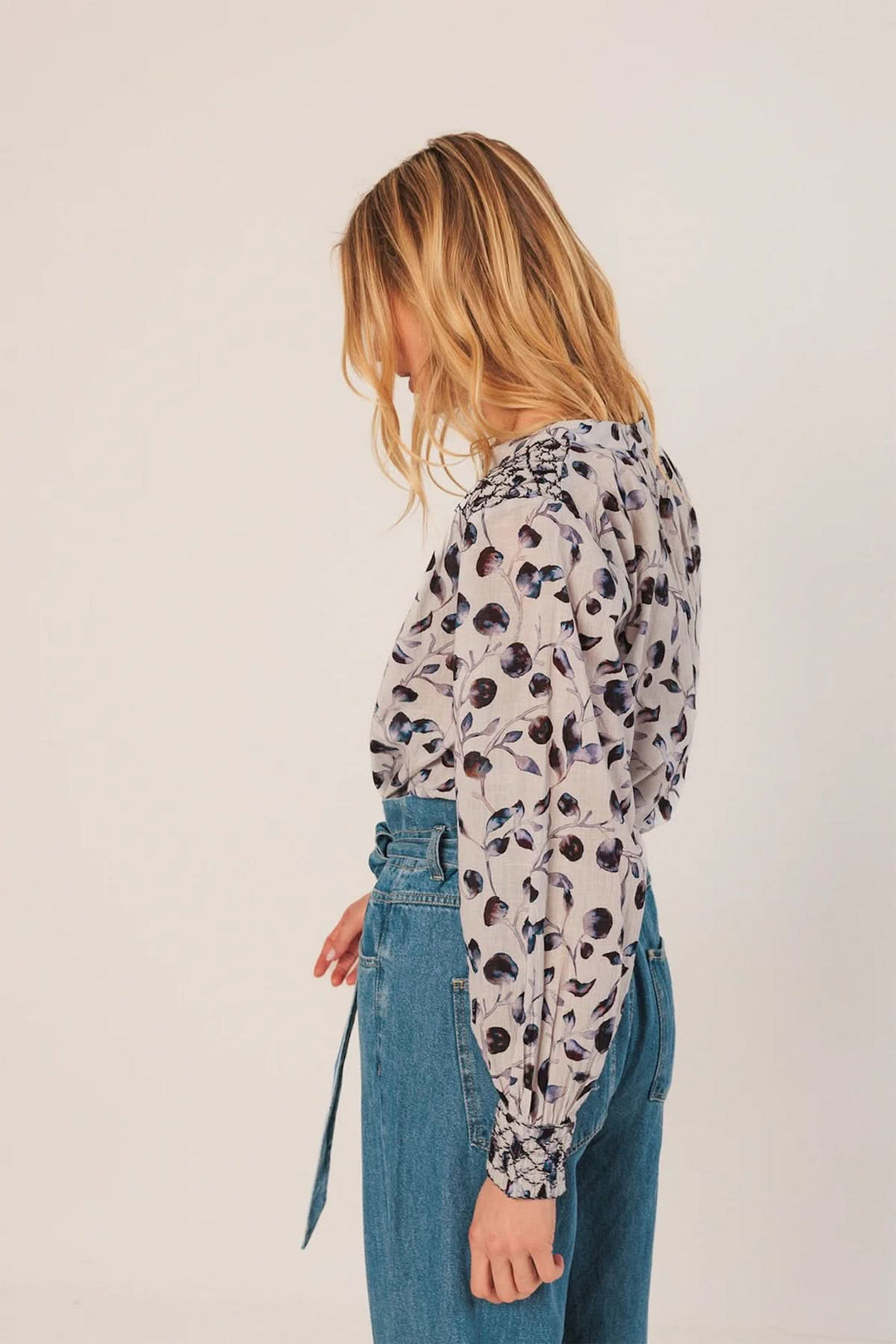 Femme portant une blouse fluide à imprimé nature avec détails smockés aux épaules, associée à un jean taille haute pour un look chic.