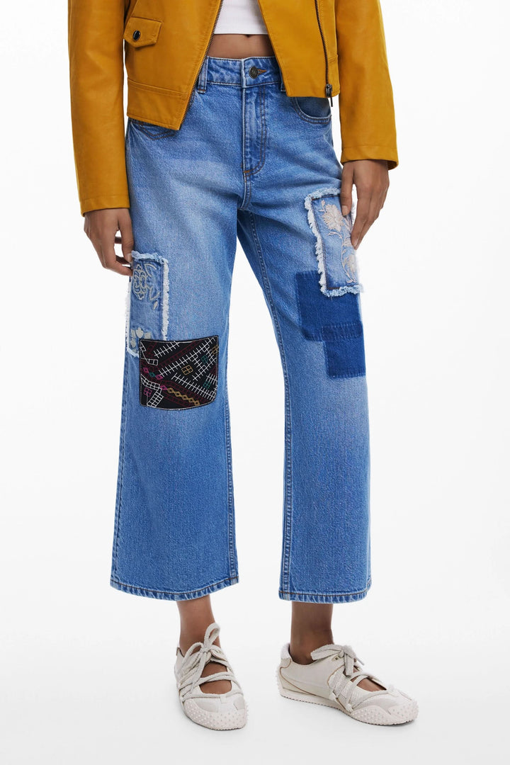 Jean à broderies avec empiècements contrastants et effet patchwork, porté avec une veste en cuir.