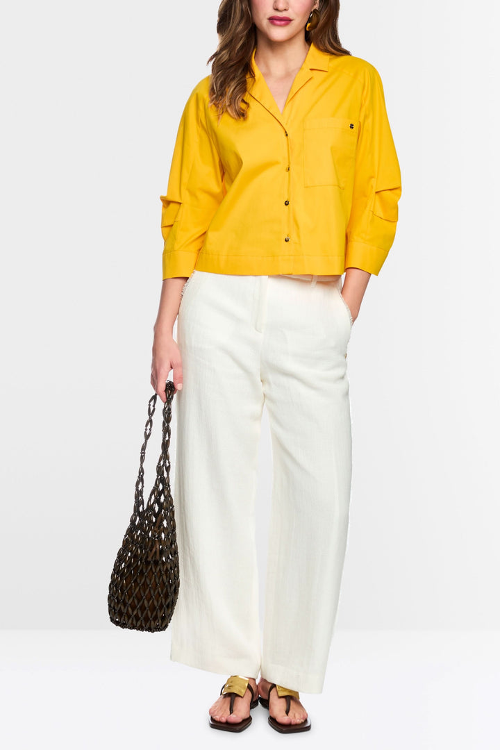 Femme portant le Pantalon WUKARI large texturé, coupe ample et élégante, avec un haut jaune et un sac en filet.
