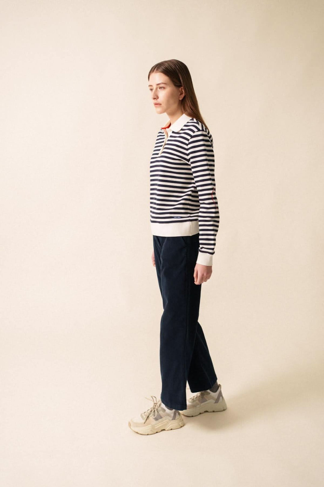 Chandail polo NINA en molleton rayé, port de profil, avec pantalon bleu marine et baskets.