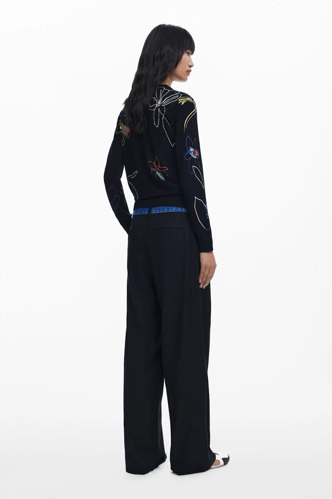 Femme vue de dos portant un chandail léger illustré à motif floral sur fond noir, avec pantalon large.