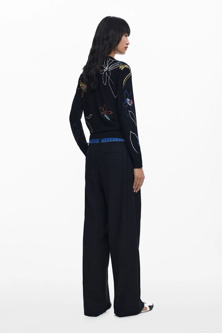 Femme vue de dos portant un chandail léger illustré à motif floral sur fond noir, avec pantalon large.