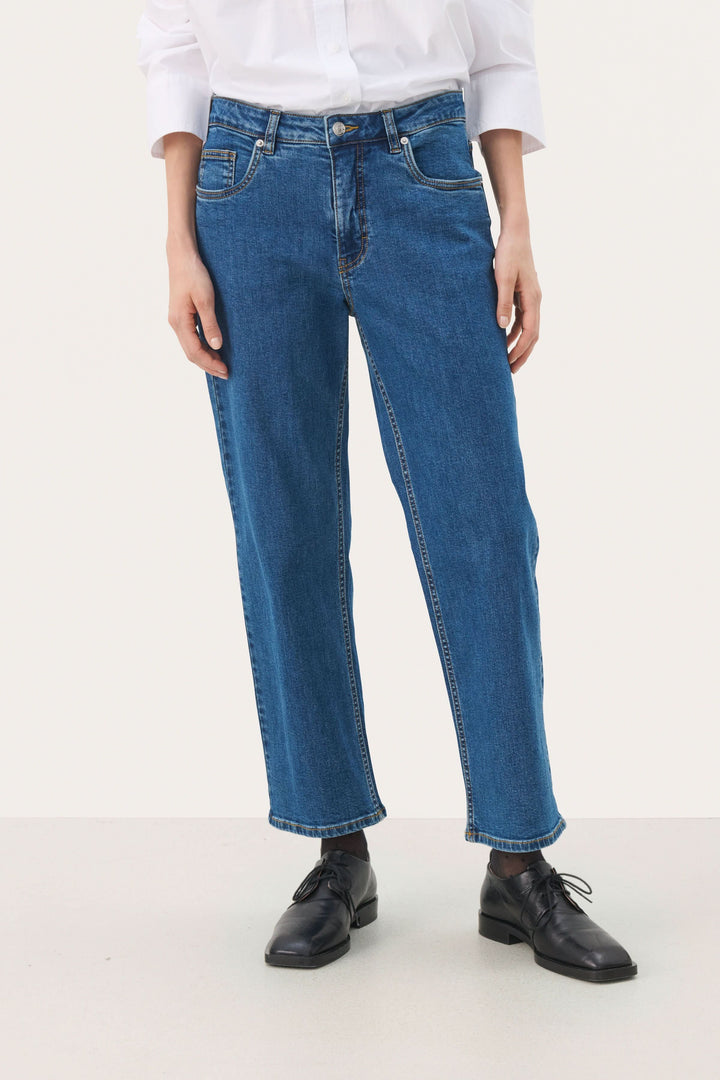 Jean à jambe droite écourtée, taille régulière, denim souple, porté avec une chemise blanche et chaussures noires.