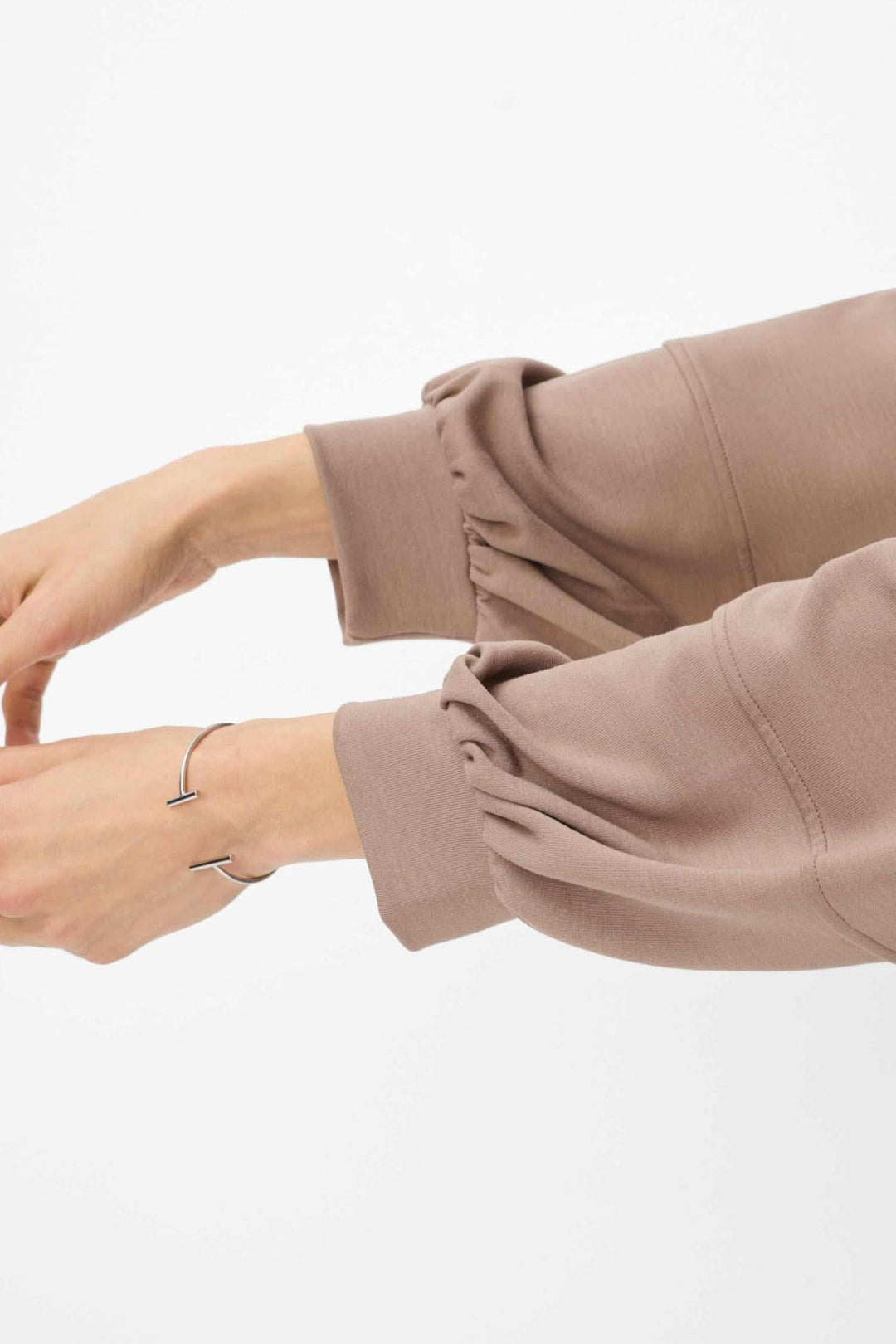 Veste Becky en tissu beige avec manches bouffantes et bracelet délicat sur un poignet.