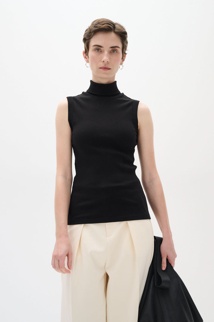 Camisole Dagna en jersey côtelé noir, col montant, sans manches, coupe ajustée, portée avec un pantalon ample.