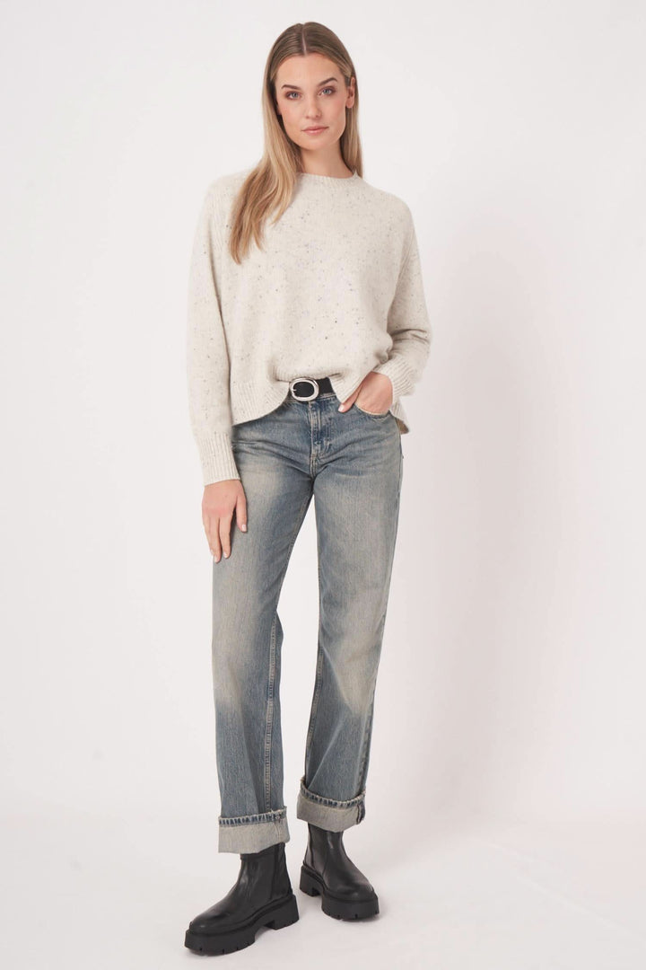 Femme portant un chandail moucheté en cachemire, jean délavé, et bottes noires, style décontracté et élégant.