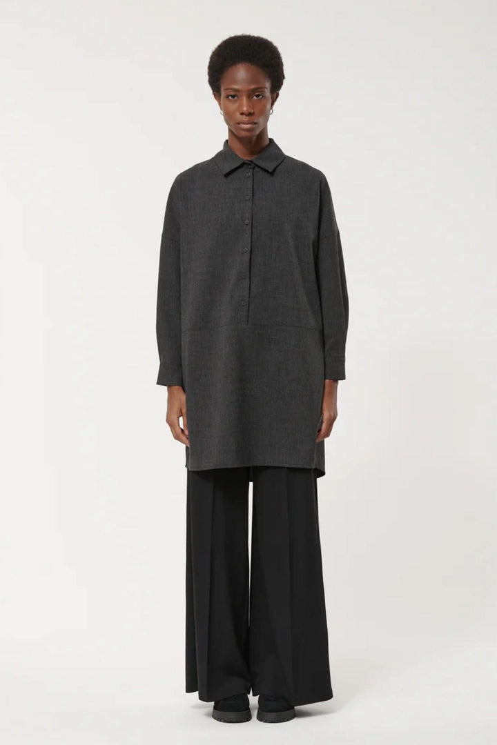 Femme portant une robe à manches longues, coupe ample, avec col classique et style minimaliste, soulignant un look élégant et moderne.