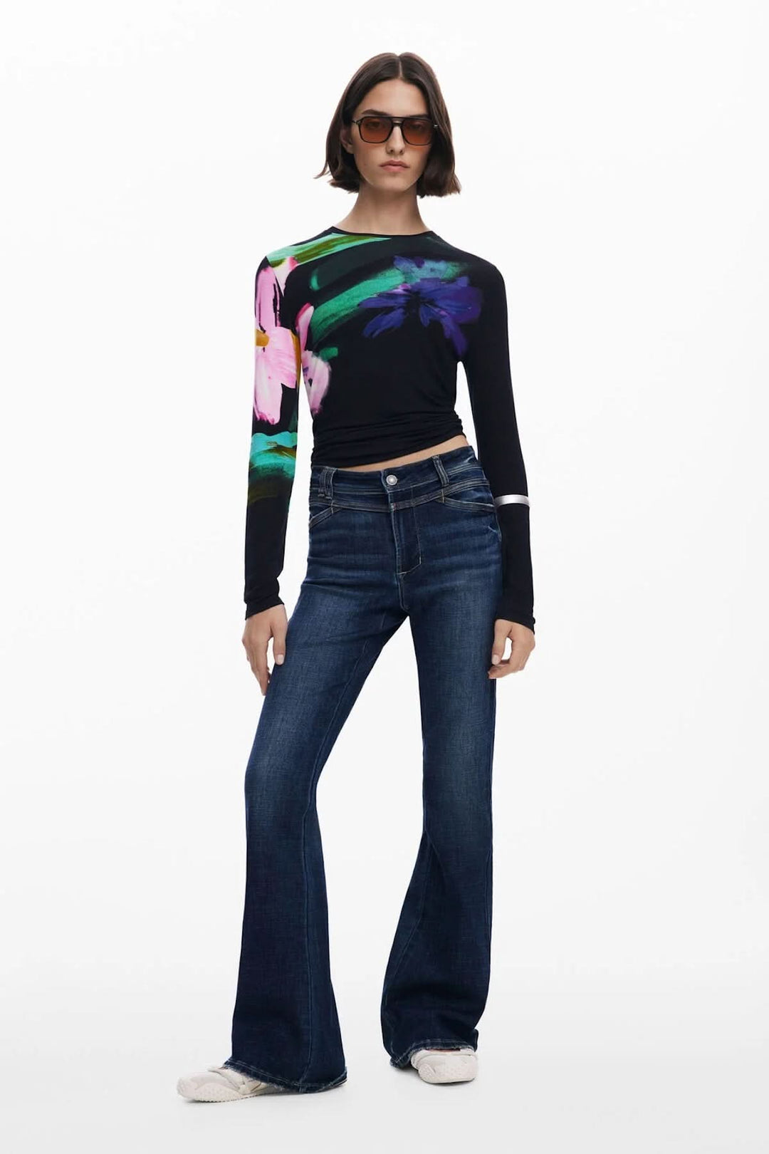Femme portant un jean évasé taille haute avec un haut à motifs floraux et des lunettes de soleil.