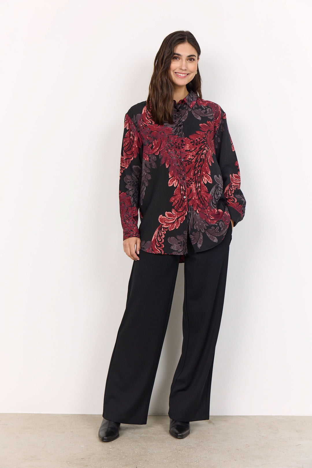 Chemise fluide à imprimé baroque en noir et rouge, portée avec des pantalons noirs larges pour un look sophistiqué.