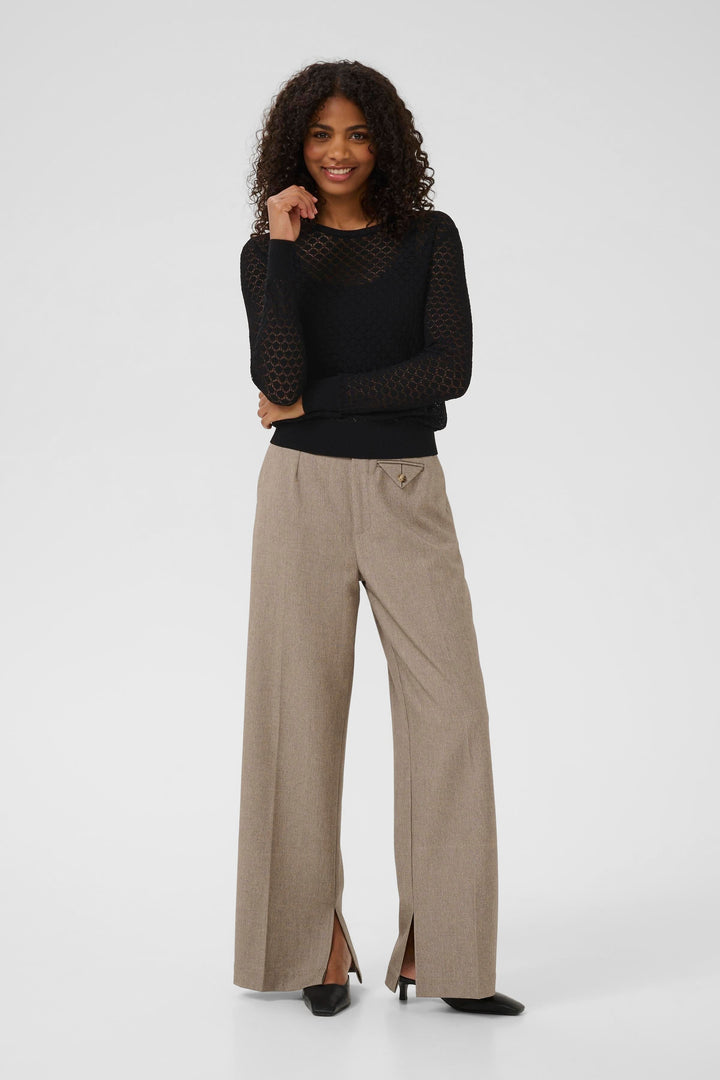Femme portant un chandail en maille ajourée noire avec des pantalons beiges à fente, look chic et sophistiqué.