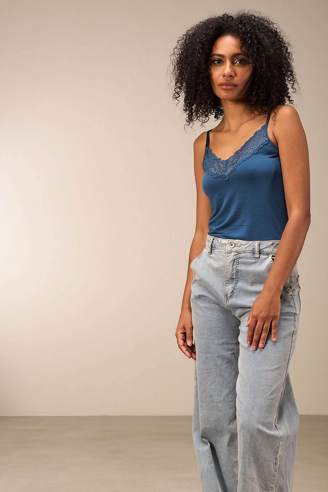 Camisole en satin bleu avec dentelle délicate, portée avec un jean clair pour un look élégant et décontracté.