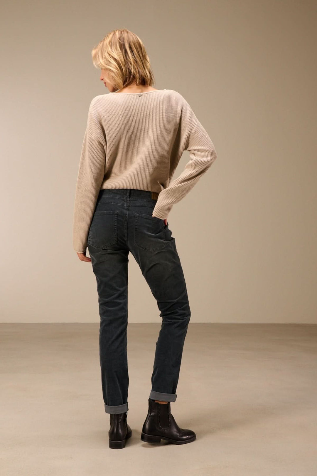 Femme portant un pantalon en velours côtelé coupe ajustée, style moderne avec bottines noires et pull beige.