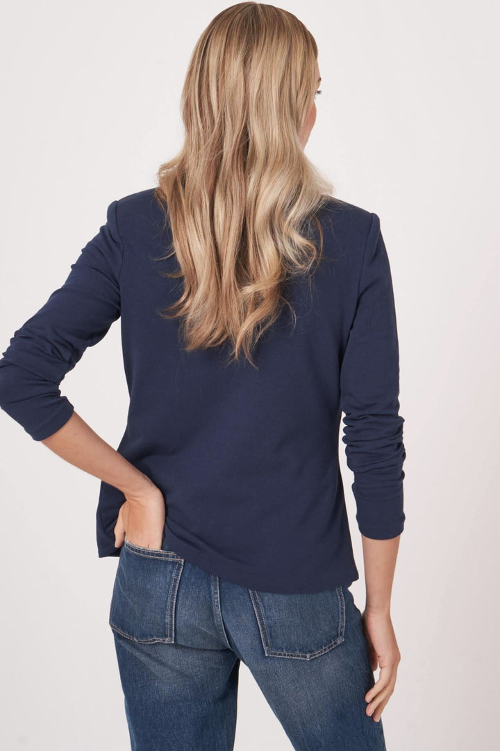 Femme vue de dos portant un veston en jersey stretch, style casual-chic, avec cheveux longs et blouson noir.