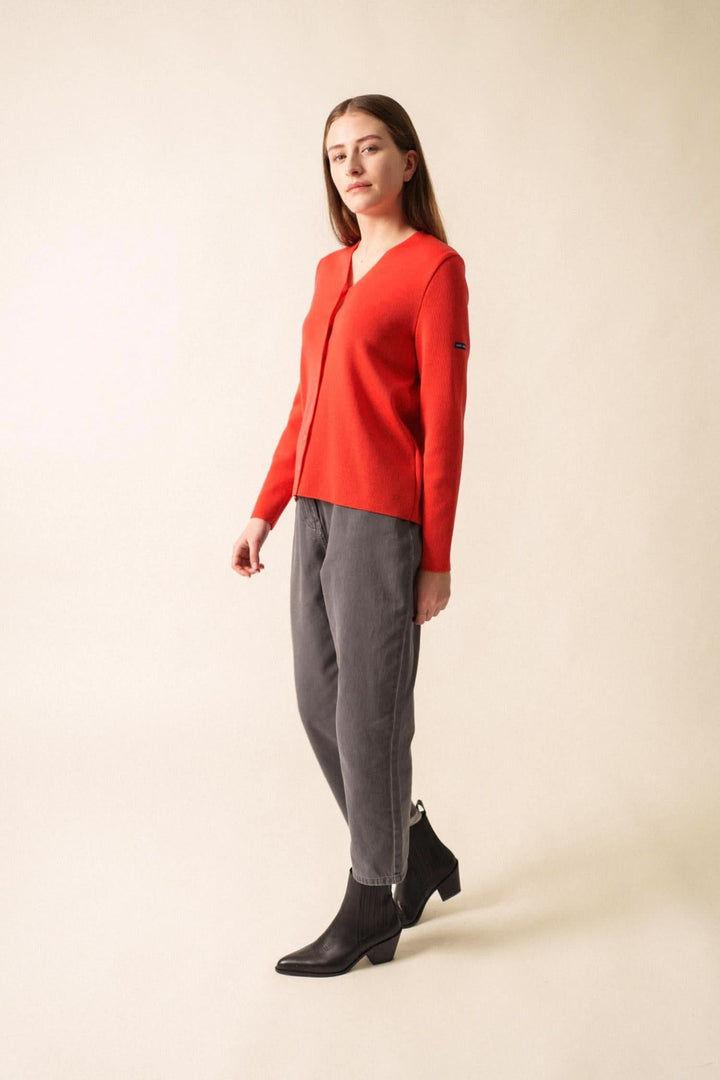 Gilet en laine rouge avec encolure en V, porté sur un pantalon gris, style chic et élégant.