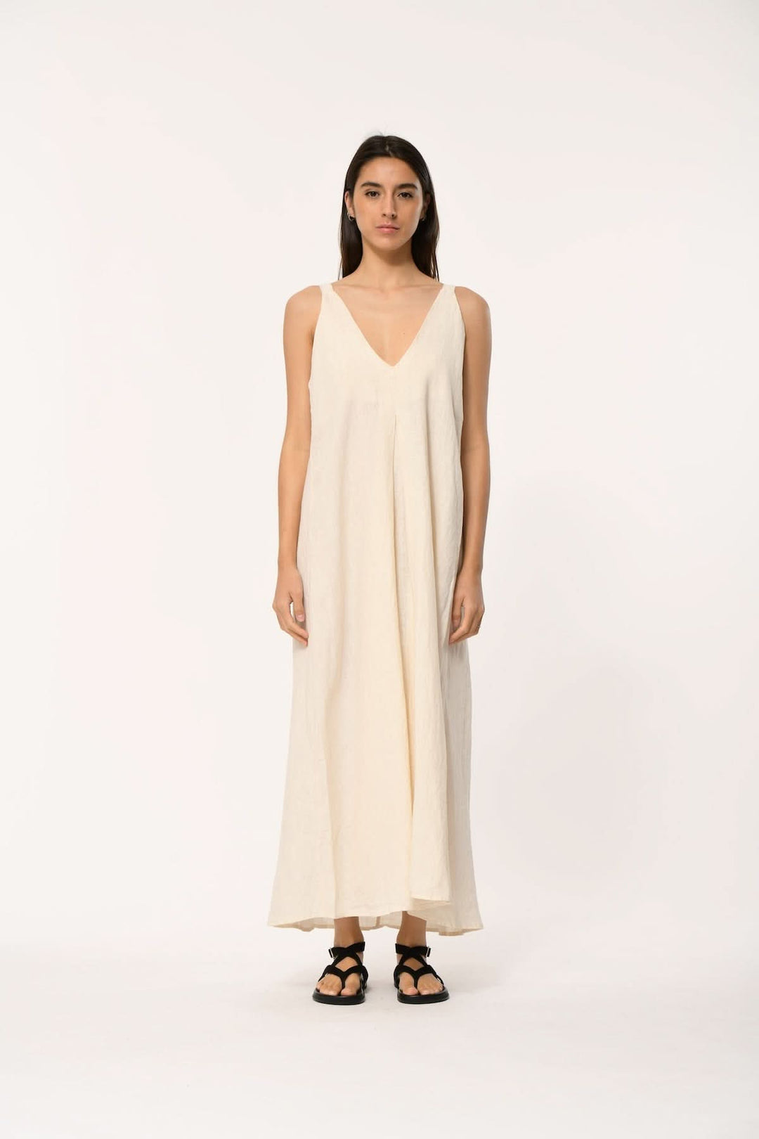 Femme portant une robe longue fluide à col v, élégante et minimaliste, avec fines bretelles, longueur longue et coupe légèrement évasée.