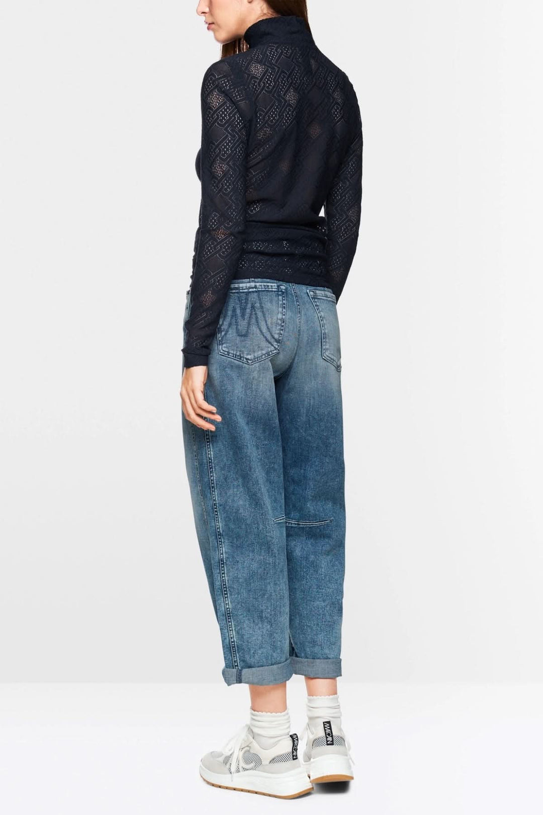 Haut en dentelle à manches longues, coupe ajustée, porté avec un jean décontracté et des baskets blanches.