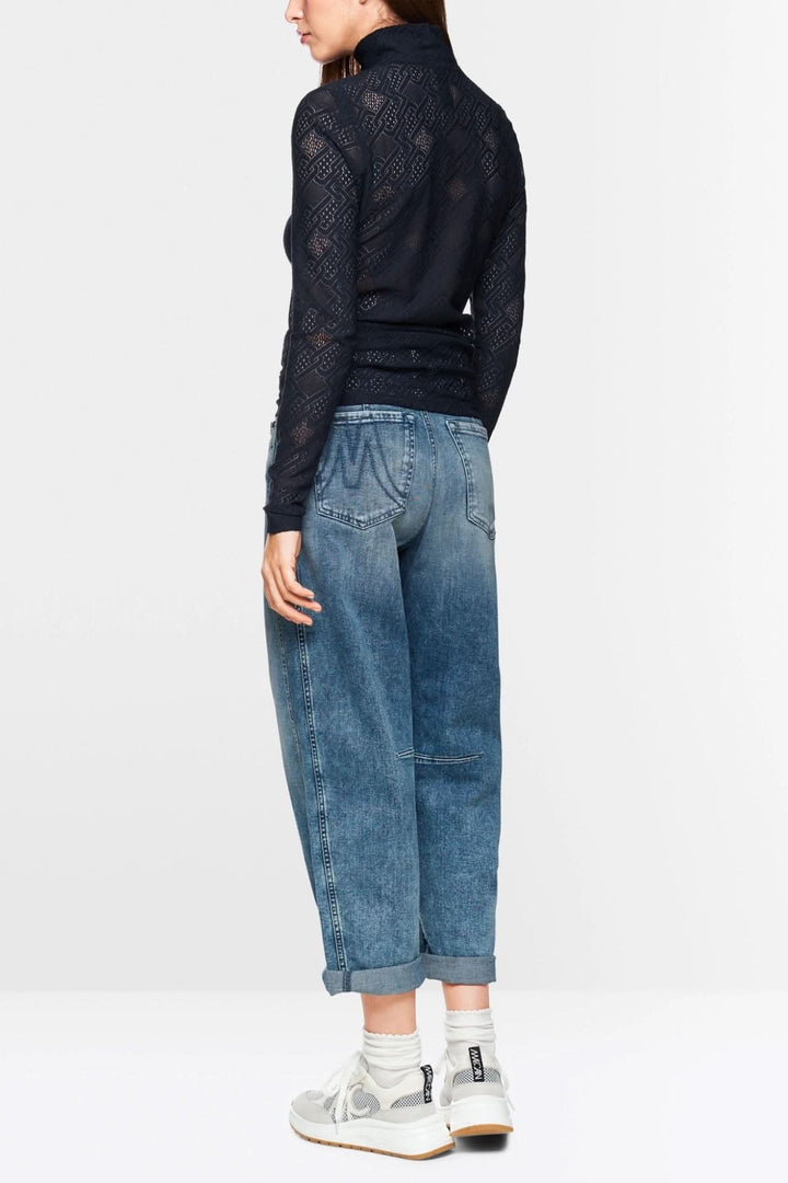 Haut en dentelle à manches longues, coupe ajustée, porté avec un jean décontracté et des baskets blanches.