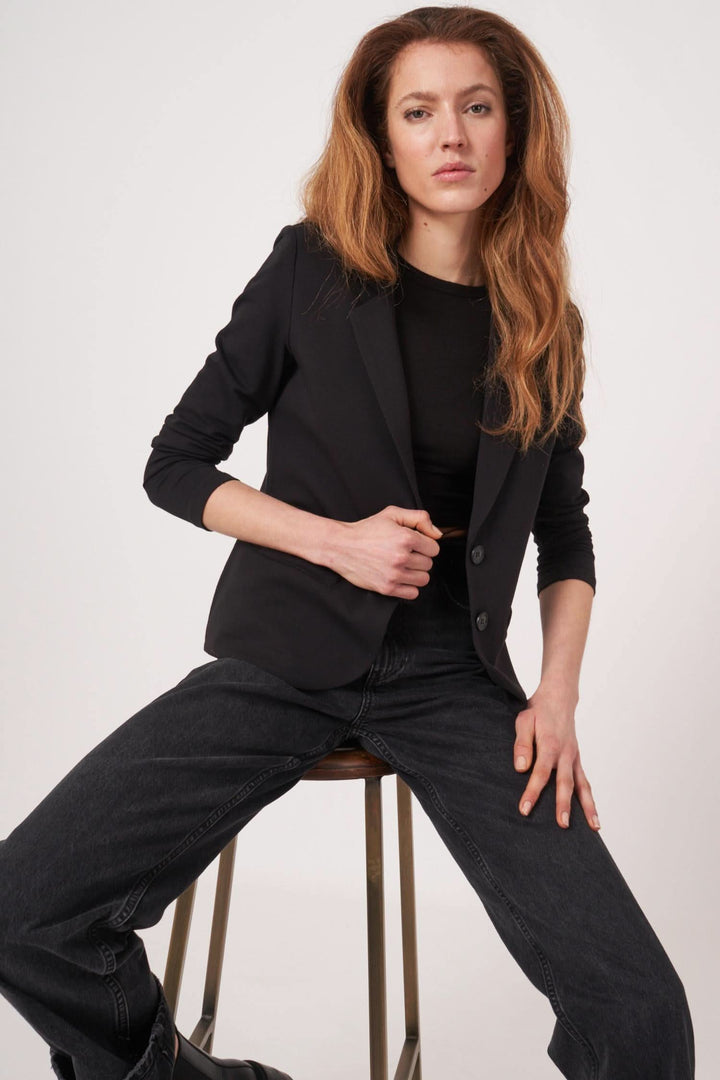 Veston en jersey stretch noir porté avec un haut noir et un pantalon large, parfait pour un look casual-chic.