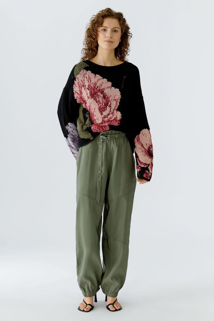 Pantalon jogger ceinturé vert avec taille élastique et ceinture intégrée, porté avec un pull à fleurs, look décontracté moderne.