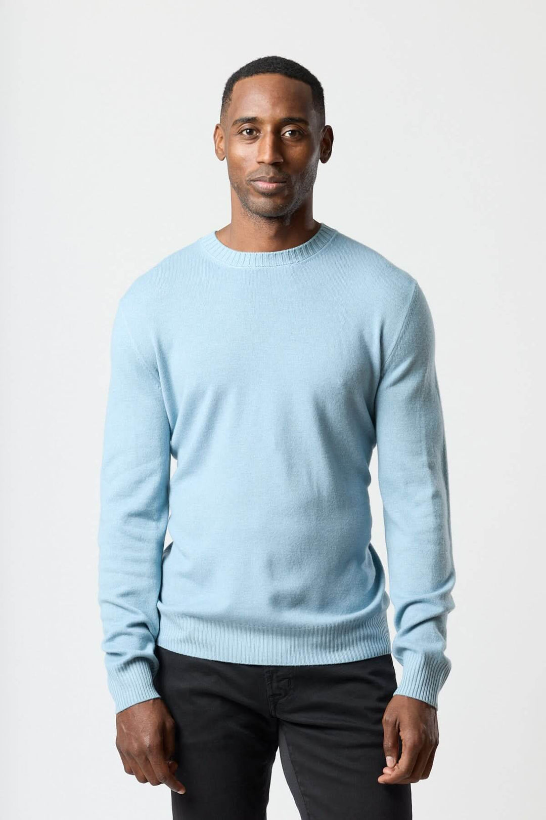 Homme portant un chandail col rond en maille douce bleu clair avec un jean noir, look moderne et confortable.