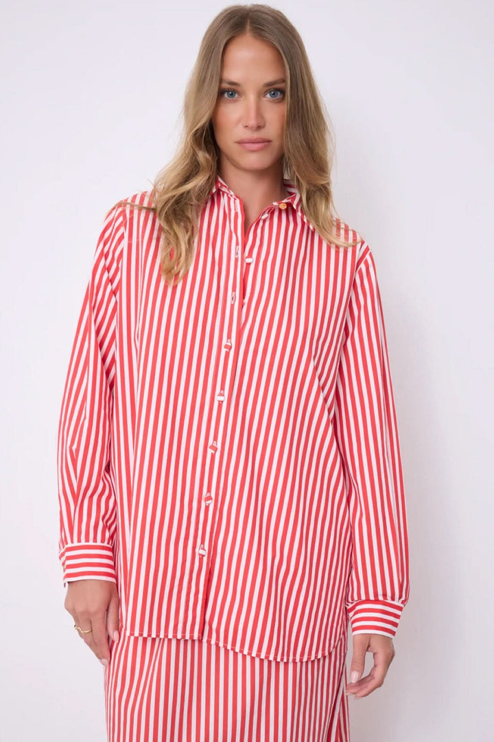 Femme portant la chemise rayée Althea coupe fluide classique rouge et blanche, à motif vertical, manches longues et col classique.