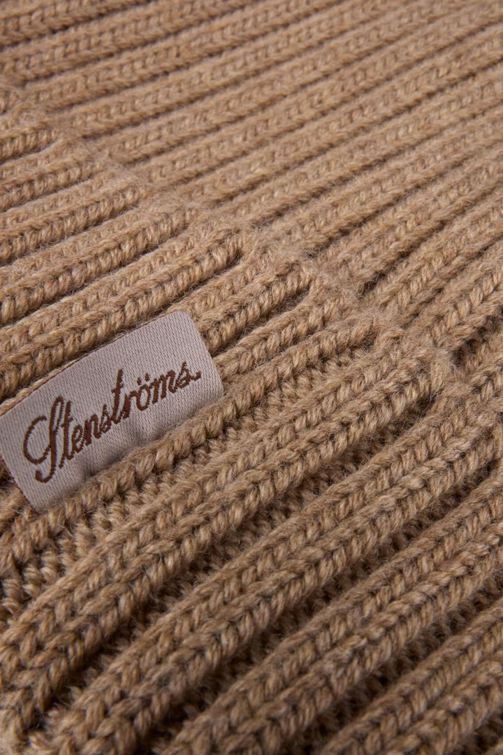 Gros plan sur une tuque en laine mérinos côtelée beige avec une étiquette de marque. Tricot chaud, extensible et élégant.