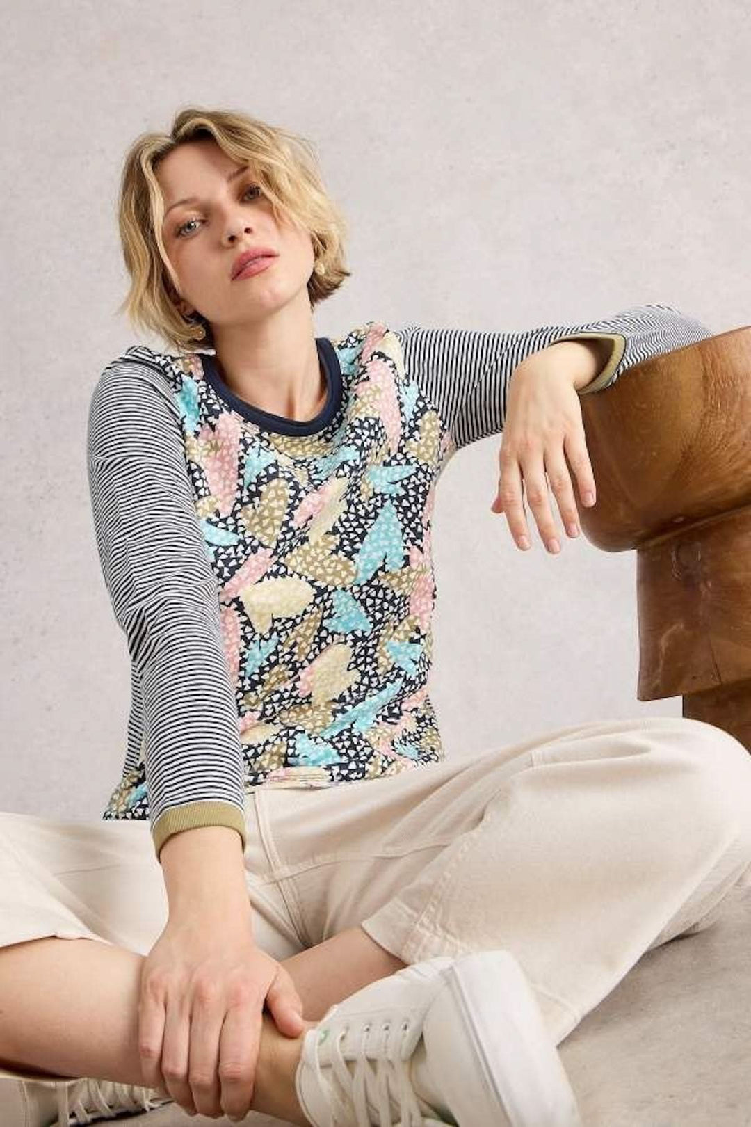 Femme portant un chandail à motifs graphiques avec imprimé floral et manches longues rayées, assise de manière décontractée.