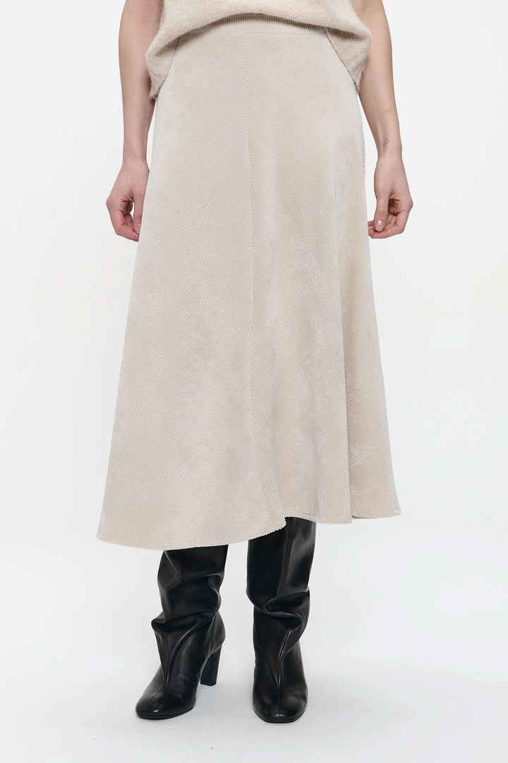 Jupe midi en velours côtelé beige avec taille haute, portée avec bottes noires pour un look élégant et moderne.