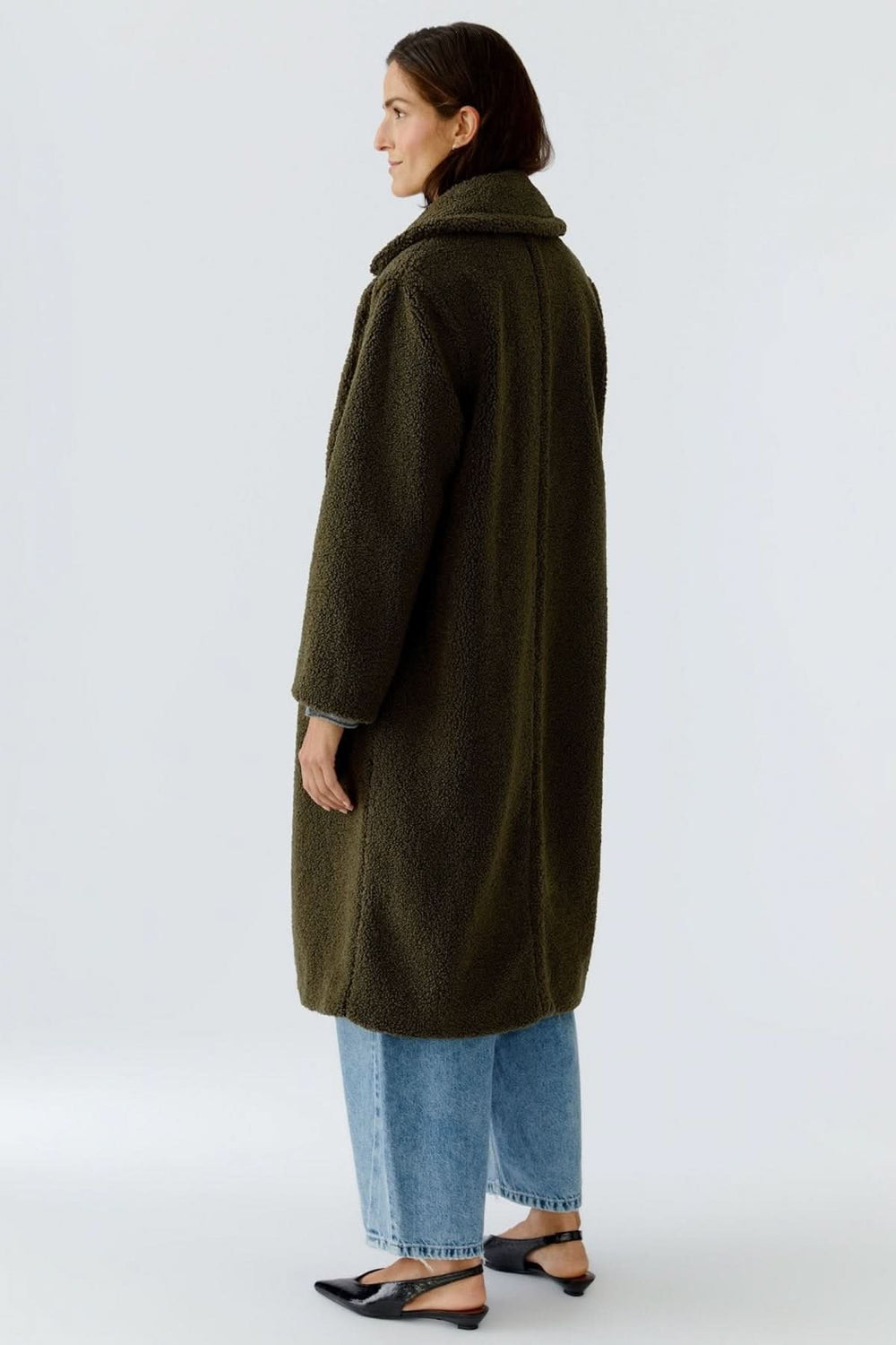 Manteau long en tissu bouclette vert foncé, porté par une femme, de dos, avec un jean et des chaussures noires.