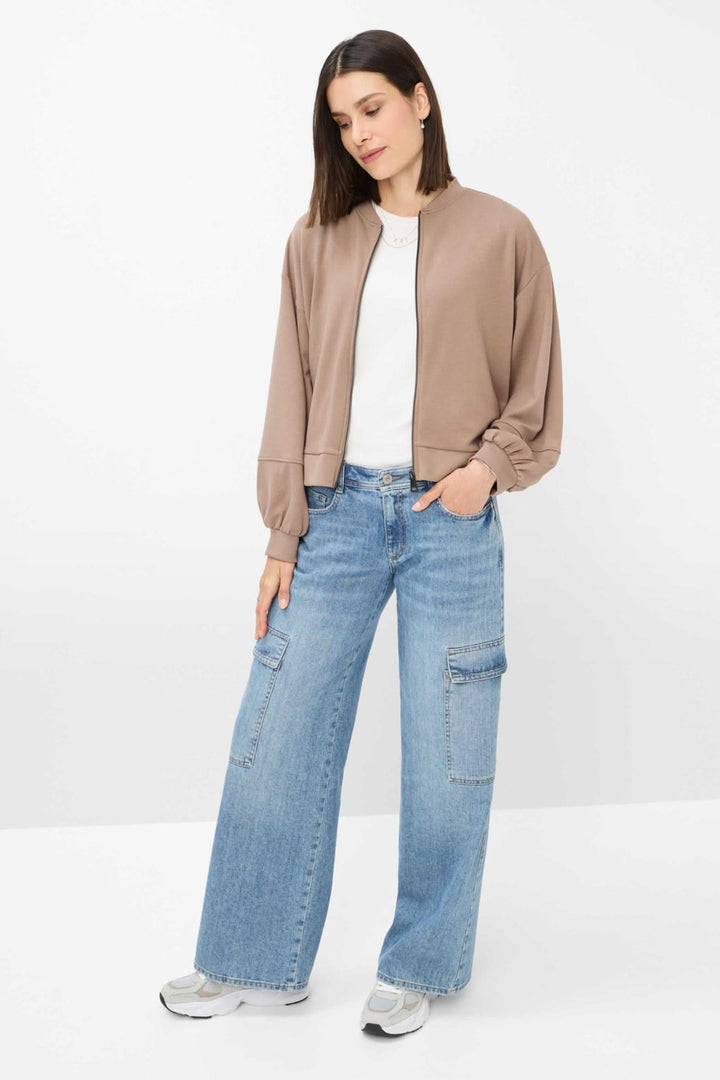 Femme portant une veste marron oversize avec un t-shirt blanc et un pantalon large en denim.