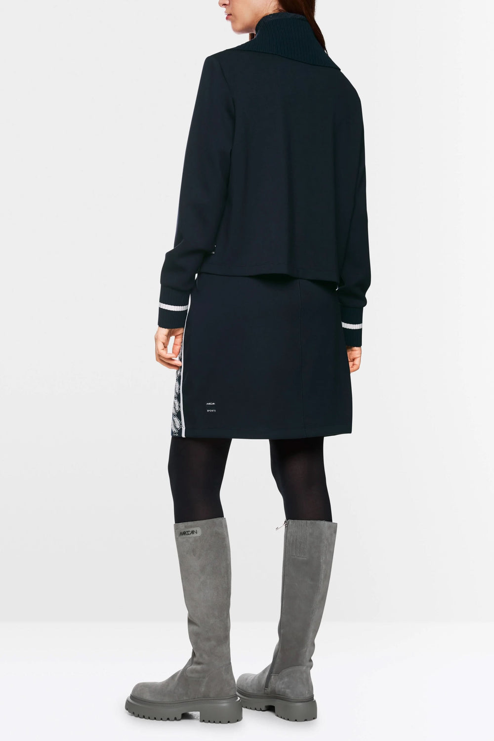 Femme vue de dos portant un cardigan zippé en maille fine, avec une jupe et des bottes, style décontracté.