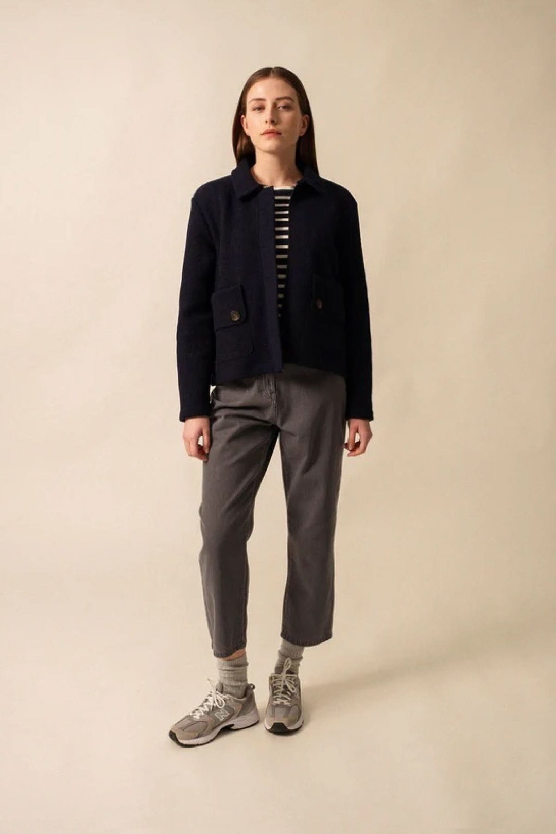 Modèle portant une veste en laine bouillie COMBLOUX, avec poches et pantalon gris, sur fond neutre.