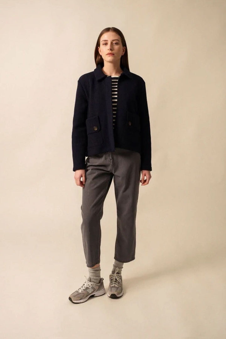 Modèle portant une veste en laine bouillie COMBLOUX, avec poches et pantalon gris, sur fond neutre.