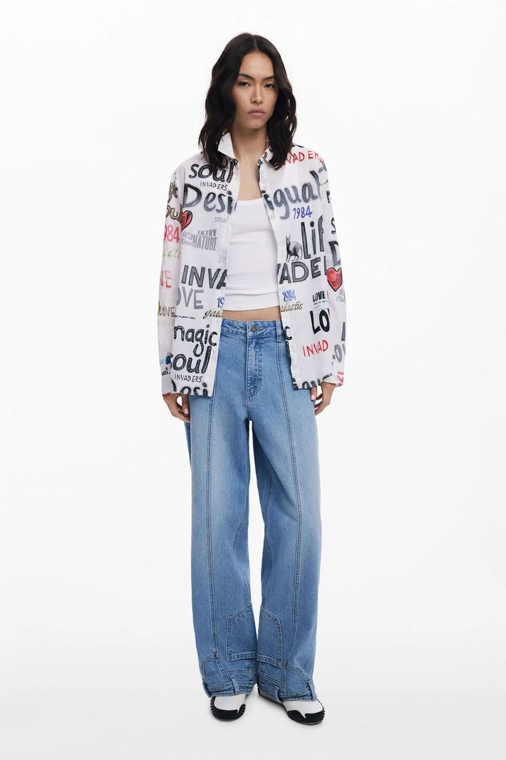 Chemisier à manches longues avec imprimé graffiti multicolore porté par un modèle, associé à un pantalon en denim.