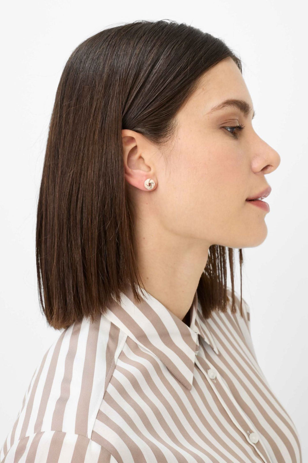 Femme portant une chemise à rayures verticales et des boucles d'oreilles, vue de profil.