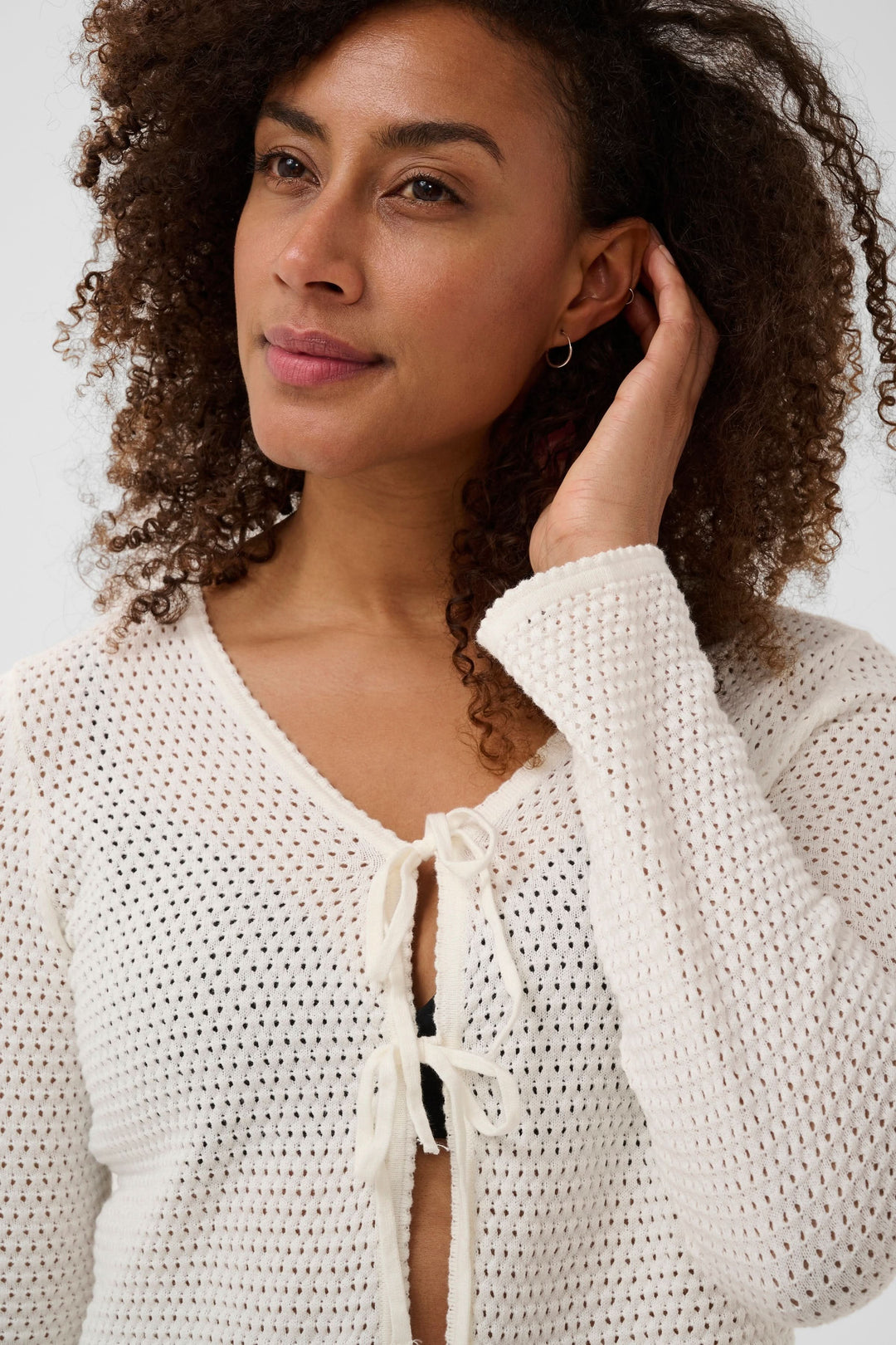 Femme portant un Cardigan Rosefina en maille ajourée à nouer avec manches longues et encolure en V, détail sur la fermeture à liens.