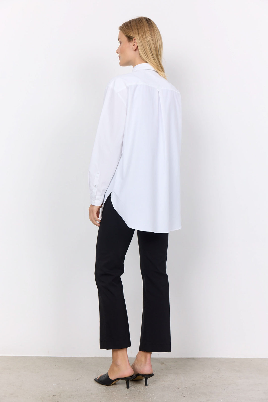 Femme portant une chemise décontractée blanche avec un pantalon noir, vue arrière, style moderne.