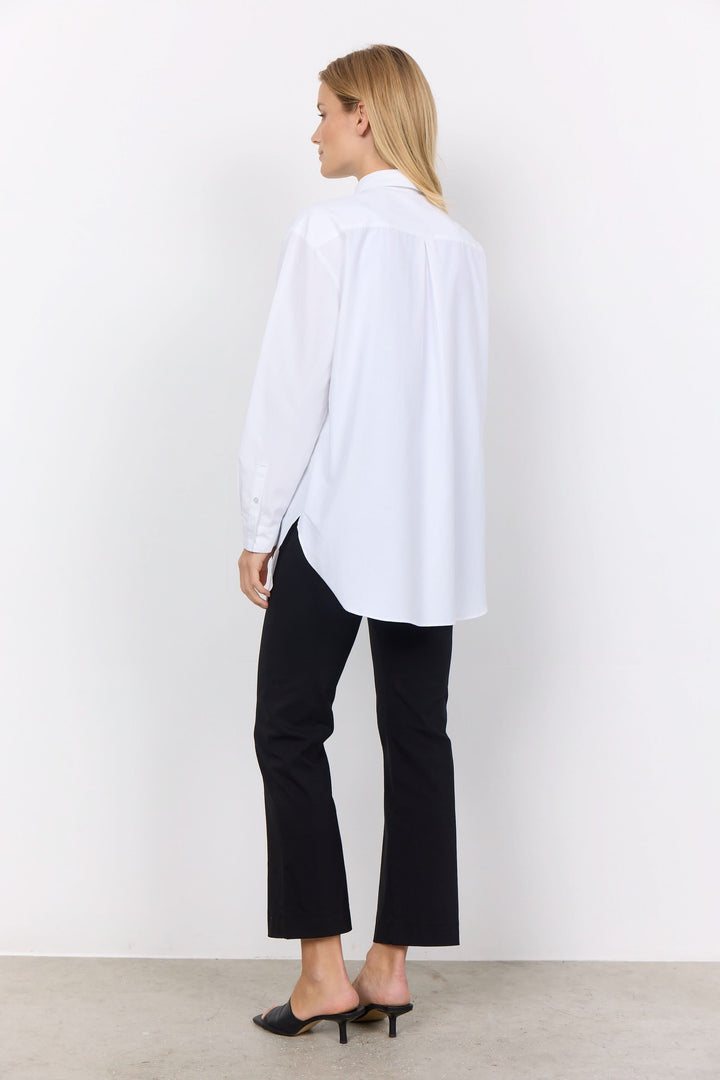Femme portant une chemise décontractée blanche avec un pantalon noir, vue arrière, style moderne.