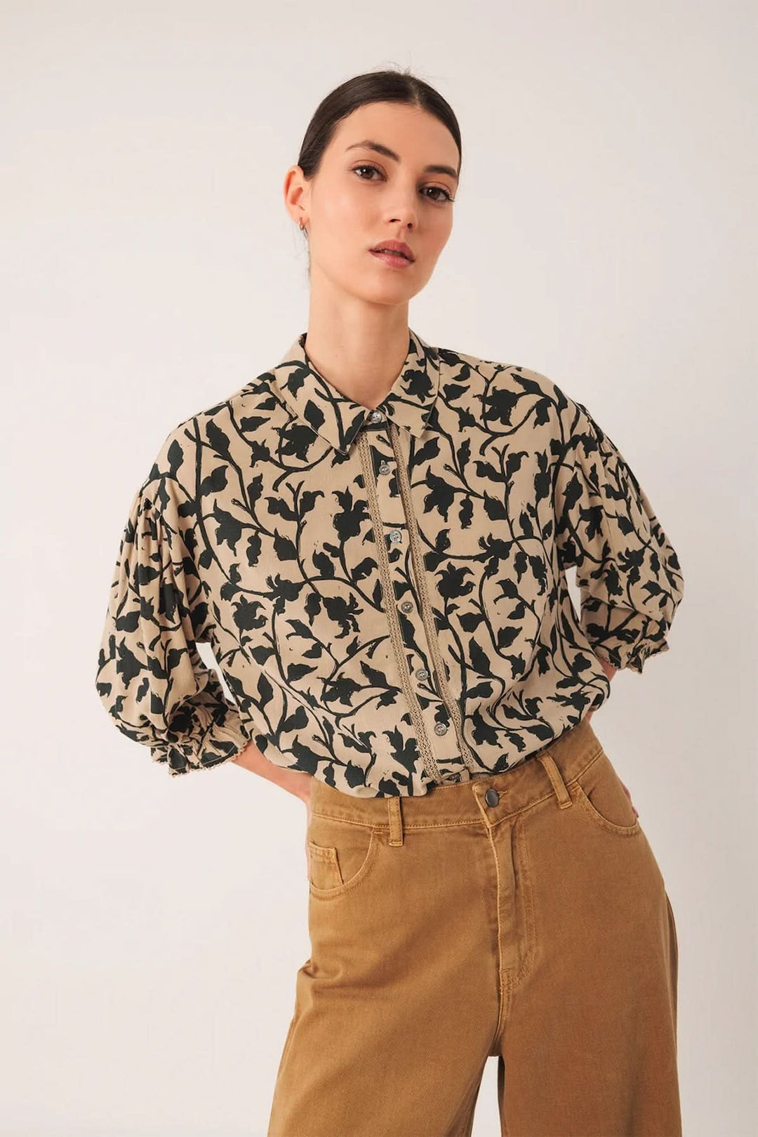 Chemise imprimée à motif végétal avec coupe fluide, col classique, manches bouffantes. Portée avec pantalon taille haute marron.